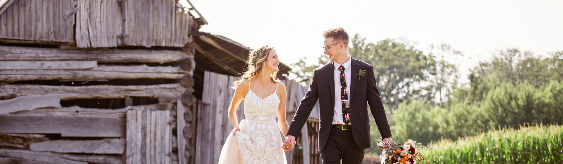Bride and groom walking in front of an old log barn